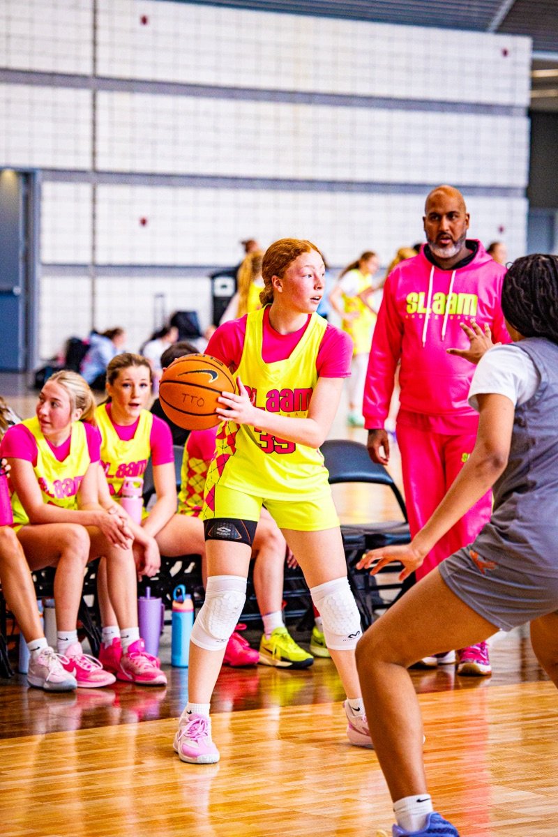 A SLAAM player handling the ball during a tournament, coaches and bench in frame.
